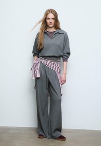 Grå strikket sweatshirt med krave, kombineret med brede grå bukser, accentueret med et rødt og hvidt stribet bælte. Glat tekstur og afslappet pasform.
