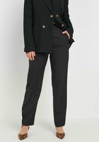 Zwarte op maat gemaakte broek met een rechte snit, lichte stof, zijzakken en een gladde textuur, gecombineerd met een zwart colbert en leoprint hakken.
