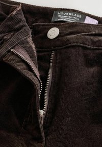 Braune Corduroy-Bootcut-Jeans mit Reißverschluss und Metallknopf; verfügt über ein strukturiertes Material und ein Etikett mit der Aufschrift "Hourglass Relaxed Bootcut."
