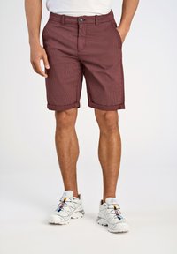 Pantaloni corti a quadri borgogna con risvolti, tasche frontali e design a punta piatta; abbinati a scarpe da ginnastica bianche.