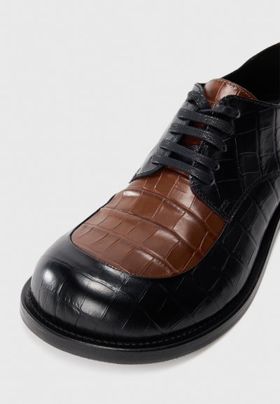 Leather dress shoe featuring a black crocodile pattern with a brown textured panel on the vamp, round toe, and black laces.