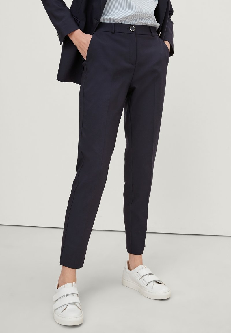 Námořnické modré kalhoty na míru se slim fit střihem, s plochým předním dílem, bočními kapsami a zapínáním na knoflík. V kombinaci s bílými teniskami.
