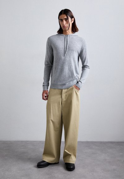 Hellgrauer Hoodie mit Kordelzug, kombiniert mit beigen weiten Hosen. Schwarze Schuhe runden das Outfit ab und weisen eine dezente Textur auf.