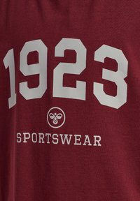 Bordowy bawełniany t-shirt z dużymi białymi cyframi "1923" oraz słowem "SPORTSWEAR" w wyrazistym fontach, a także okrągłym logo.