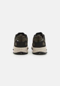 Chaussures de sport noires et vert foncé avec un dessus texturé et une semelle beige mouchetée, présentant un design tissé et une languette à l'arrière.