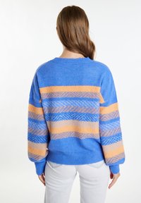 Mėlynai ir oranžiškai dryžuotas megztinis su tekstūriniais raštais, apvalia iškirpte ir ilgomis, laisvai krentančiomis rankovėmis. Medžiaga atrodo minkšta ir pūkuota.