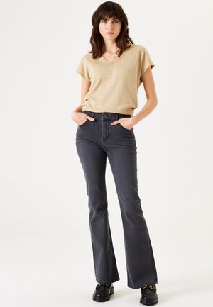Haut beige à manches courtes en V associé à un jean évasé gris foncé. Le jean a une taille ajust�ée et des poches avant, porté avec des chaussures noires.