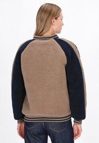 Tan og marineblå fleecejakke med raglanærmer, ribstrikst krave og manchetter samt blød tekstur; har en afslappet pasform og et afslappet design.