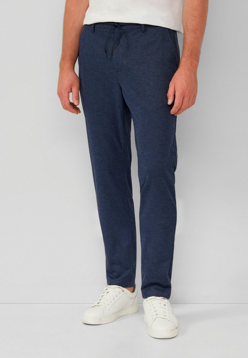 Marineblaue Jogginghosen aus strukturiertem Stoff mit einem elastischen Bund und Kordelzug. Kombiniert mit weißen Sneakers.