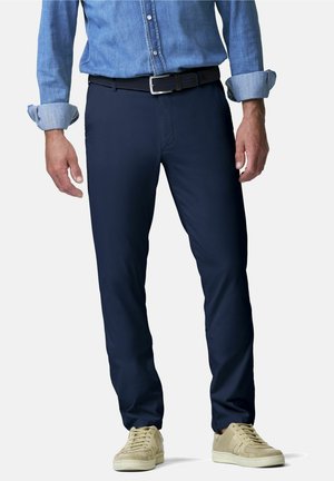 Homme portant un pantalon bleu foncé, des baskets beige clair et une chemise en denim à manches longues retroussées avec une ceinture noire.