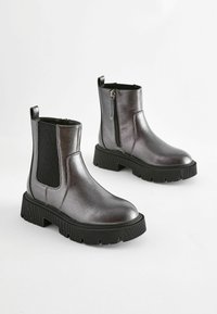 Bottines métalliques grises avec des panneaux élastiques sur les côtés, fermeture éclair et semelles en caoutchouc noir épaisses avec un motif de traction texturé.