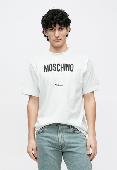 Biały bawełniany t-shirt z wyraźnym czarnym napisem "MOSCHINO" i napisem "Milano" poniżej. Krótkie rękawy, luźny krój. Połączony z jasnoniebieskimi dżinsami.