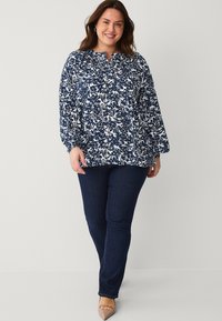 Marineblauwe en witte bloemenpatroon blouse met geplooid detail bij de halslijn, lange mouwen, gecombineerd met donkerblauwe jeans en beige schoeisel.