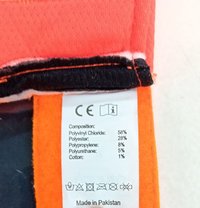 Label with a white background, featuring black text detailing fabric composition: Polyvinyl Chloride (58%), Polyester (28%), others. Bright orange and black accents.