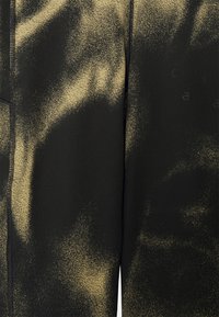 Calças de treino pretas com um padrão texturizado de manchas douradas. O tecido parece suave com costura ao longo das costuras.