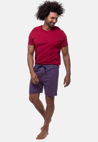Rød kortermet T-shirt parret med navy og hvidstribede badeshorts, der har elastisk talje og snørre, båret barfodet.