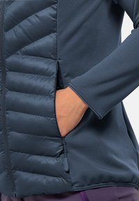 Marineblaues Jacket mit gestepptem Innenfutter auf der einen Seite, glattem Stoff auf der anderen, mit Reißverschlusstaschen und taillierten Ärmeln.