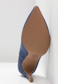 Chaussure à talons hauts en daim bleu avec un bout pointu et un talon étroit, dotée d'une semelle en cuir marron lisse et de marquages de taille en relief.