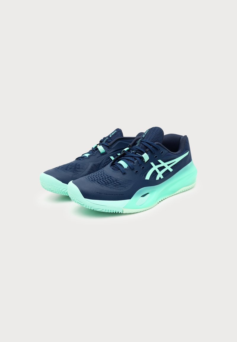 Paire de chaussures de sport bleu marine et vert menthe avec lacets et semelles rembourrées sur un fond clair uni.