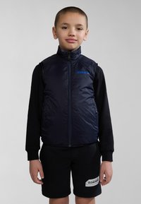 Marinblå pufferväst med hög krage och blått logotyp, bärs över en svart långärmad tröja; matchas med svarta shorts med en vit logotyppatch.
