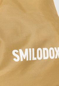 Bolsa de tela dorada con superficie texturizada y logo "SMILODOX" impreso en blanco. El material parece duradero y flexible.