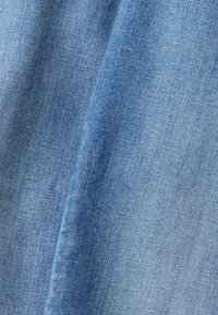 Tela de mezclilla en azul claro con una textura suave. Presenta un patrón de tejido clásico y ligeras variaciones de color a lo largo.