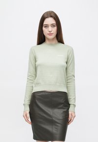 Vaaleanvihreä neulottu villapaita pyöreällä pääntiellä ja resorireunuksilla, yhdistetty istuvaan mustaan nahkahameeseen. Yksinkertainen ja moderni muotoilu.