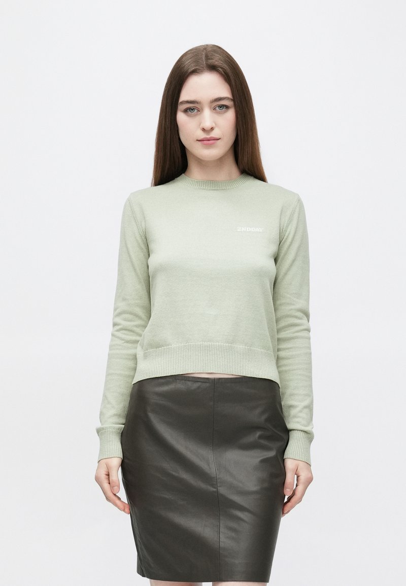 Vaaleanvihreä neulottu villapaita pyöreällä pääntiellä ja resorireunuksilla, yhdistetty istuvaan mustaan nahkahameeseen. Yksinkertainen ja moderni muotoilu.