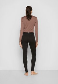 Bruine lange mouwen top met raglanmouwen, gecombineerd met zwarte leggings met een brede tailleband en flatlock naden. Gladde textuur.