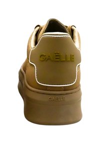 Sneaker marrone con una texture liscia, dotato di un'etichetta sul tallone con marchio e dettagli bianchi. Il design presenta bordi arrotondati e una suola spessa.