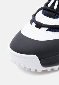 Λεπτομέρεια αθλη τικού παπουτσιού σε ασπρόμαυρο με υφασμάτινη υφή στο επάνω μέρος, αντίθετο ύφασμα και εμφανή κορδόνια. Στρογγυλεμένη μύτη και καλουπωμένη σόλα.