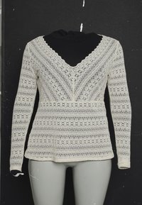 Haut à manches longues en dentelle avec un col en V, des motifs complexes en blanc cassé, et un design superposé sur un col roulé noir.