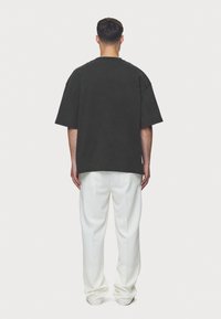 Oversized dark gray t-shirt with a relaxed fit, featuring wide short sleeves and a round neckline, paired with cream-colored trousers.