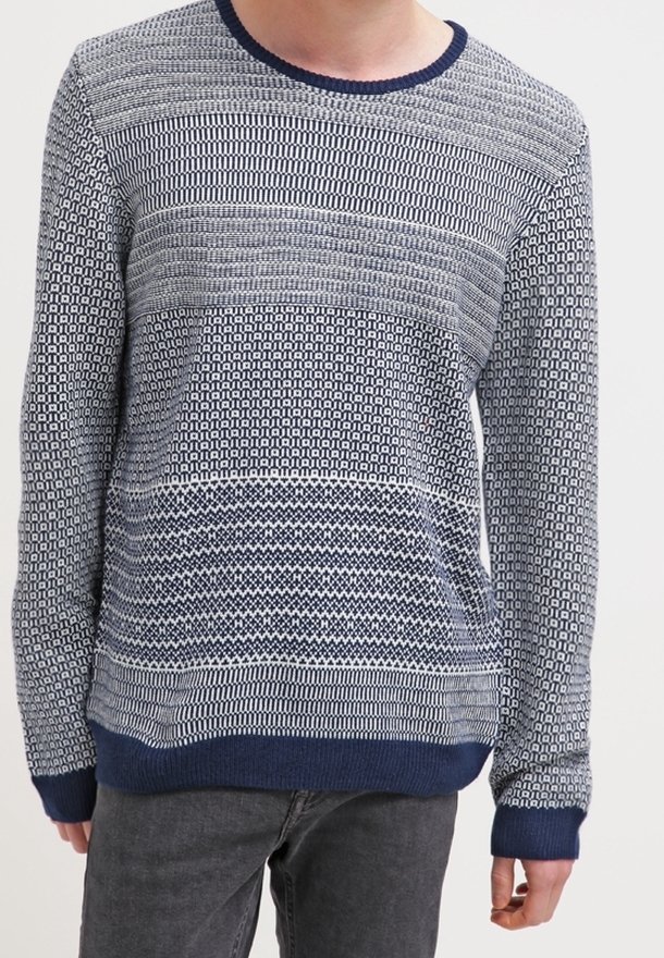Homme portant un pull à manches longues en maille avec des motifs géométriques bleus et blancs et des poignets et un ourlet bleu foncé.