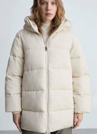 Beige gewatteerde jas met een ritssluiting aan de voorkant, capuchon en elastische manchetten. Heeft horizontale stiksels en een gladde, glanzende textuur.