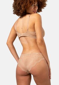 Beige spetsunderkläder med vågformad design. Bh:n har justerbara axelband och en hyskspänning. Mjuk textur med intrikata detaljer.