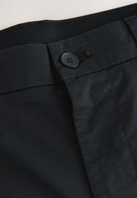 Black cotton fabric with a smooth texture, featuring a front button closure, and stitched accents at the waistline for secure fit.