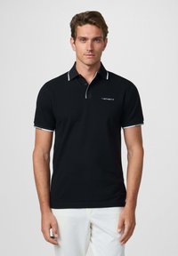 Camisa polo negra con acentos blancos, de manga corta y cuello de dos botones, con un logo en el lado izquierdo del pecho. Textura suave.