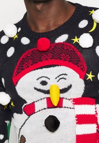 Strickpullover mit einem Schneemannmuster. Dunkler Hintergrund mit weißen Punkten, roter und weißer gestreifter Schal und bunten Bommel.