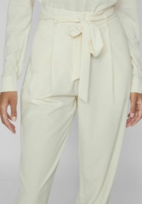 Kreemikaalased kõrge vöökohaga püksid, mis on valmistatud siledast kangast, koos vöödeta detailiga, millel on sõlm ja eesmine volt, lisades tekstuuri.