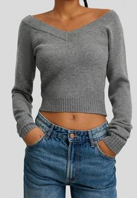 Grå kortärmad tröja med off-shoulder-design, ribbad halsringning och muddar; matchad med högmidjade blå jeans med fickor och knapp.