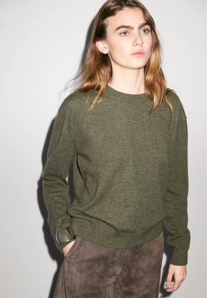 Olive green sweater with round neckline and long sleeves, made from a soft knit material, paired with brown suede pants.