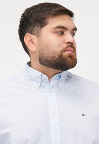 Jasnoniebieska koszula z długim rękawem z delikatnym geometrycznym wzorem, z kołnierzykiem zapinanym na guziki i małym logotypem marki na piersi.