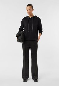 Czarna bluza z kapturem na sznurek i ściągaczami na rękawach, zestawiona z czarnymi, dopasowanymi spodniami. Po bokach trzymana pikowana torebka o fakturze.