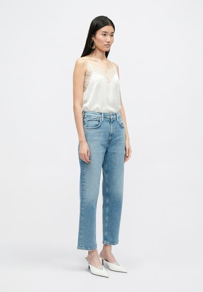 Top din satin cu guler cowl, accentuat cu dantelă transparentă, asortat cu blugi drepți albaștri deschiși și mule albe cu toc. Design simplu și curat.