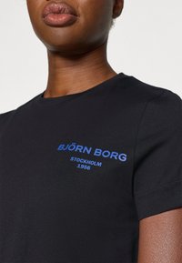 Juoda trumpų rankovių marškinėliai, pagaminti iš lygios medvilnės. Krūtinėje yra mėlyna spauda "BJÖRN BORG STOCKHOLM 1956". Klasikinio apvalaus kaklo dizainas.