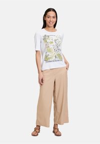 Hvid kortærmet t-shirt med et blomster grafisk design, parret med beige vidde bukser og brune remsandaler.