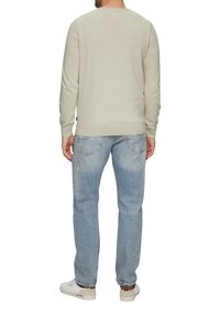 Hellgrauer Strickpullover mit geripptem Saum, kombiniert mit hellblauen Jeans. Die Jeans haben einen strukturierten Stoff und leichte Waschungen. Weiße Turnschuhe inklusive.