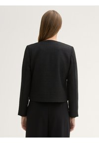 Chaqueta negra texturizada con escote redondeado, mangas largas y un corte corto. La tela tiene un patrón sutil y no tiene adornos.