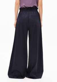 Weite Hosen aus marineblauem Stoff mit elastischem Bund und Seitentasche, glatte Textur ohne sichtbare Muster.